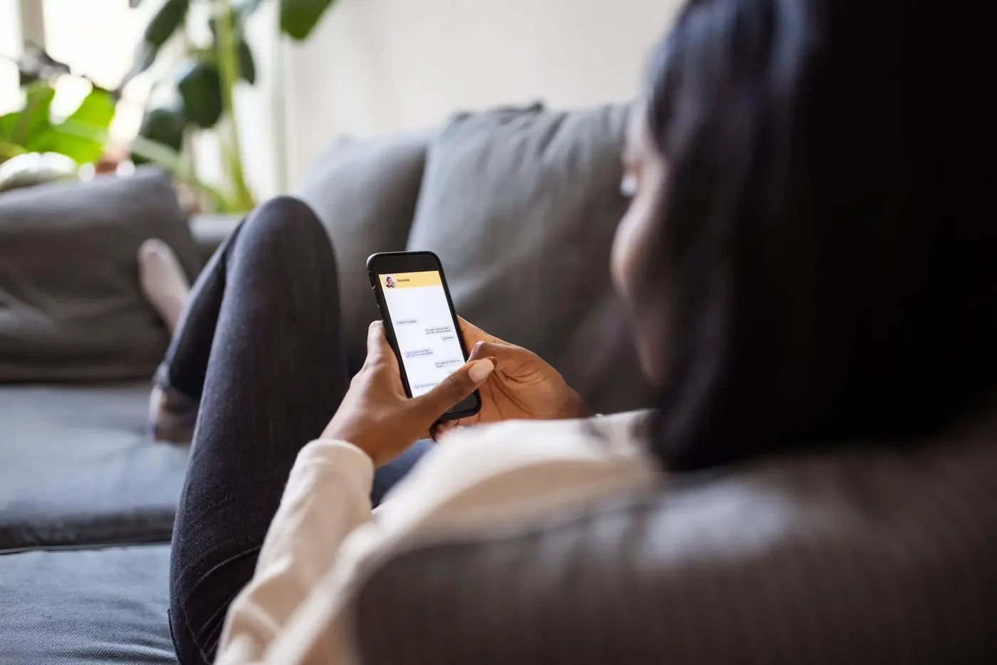A woman relaxing on a sofa, typing a message on her phone